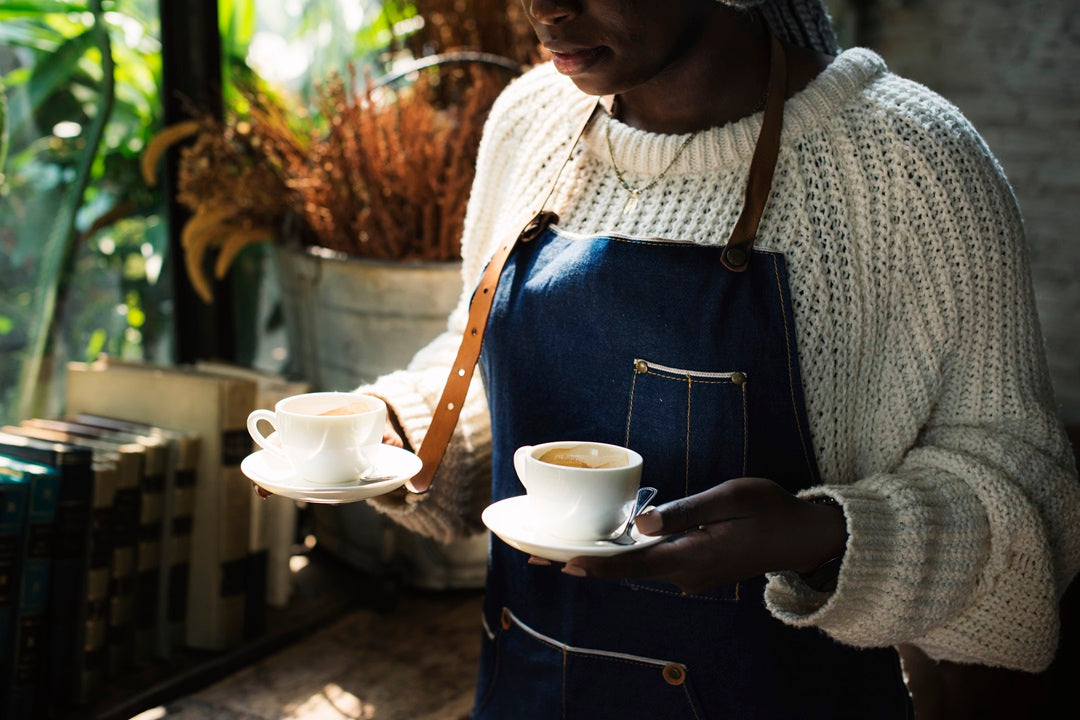 A barista holding two different cups of coffee.